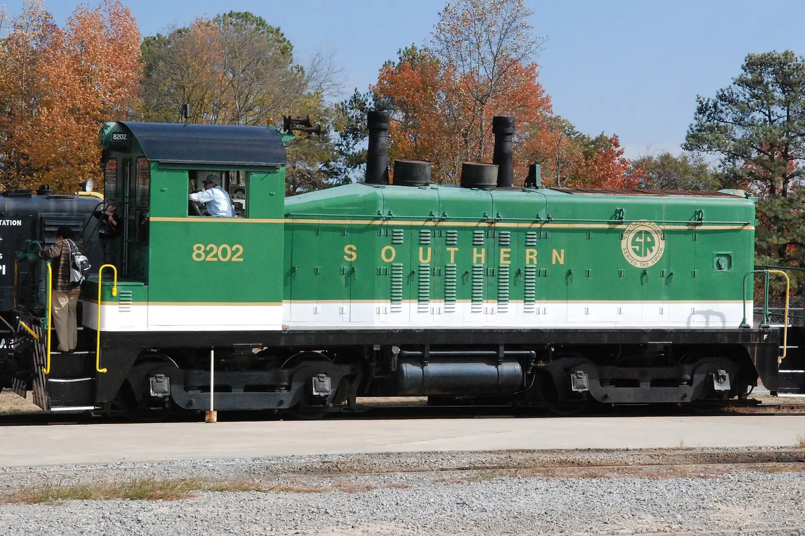 A green Southern Railway switcher locomotive under fall trees at the Southeastern Railway Museum in Duluth